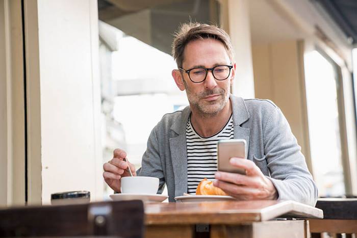 man sitting at sidewalk cafe with smart phone