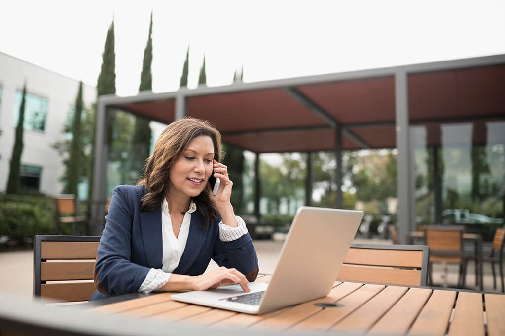 Hispanic woman using laptop and talking on cell phone