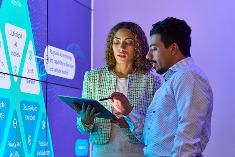 Two professionals analyzing data on screens with a tablet, promoting AI in Healthcare eBook by IQVIA for secure, responsible AI adoption.