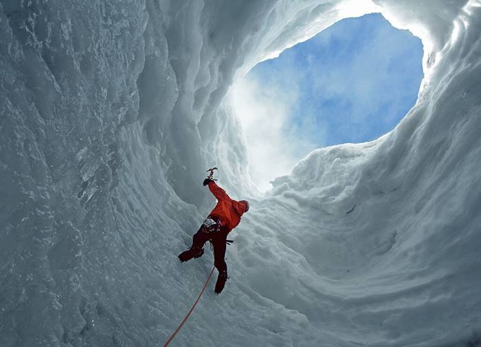 man climbing glacier with ice pick